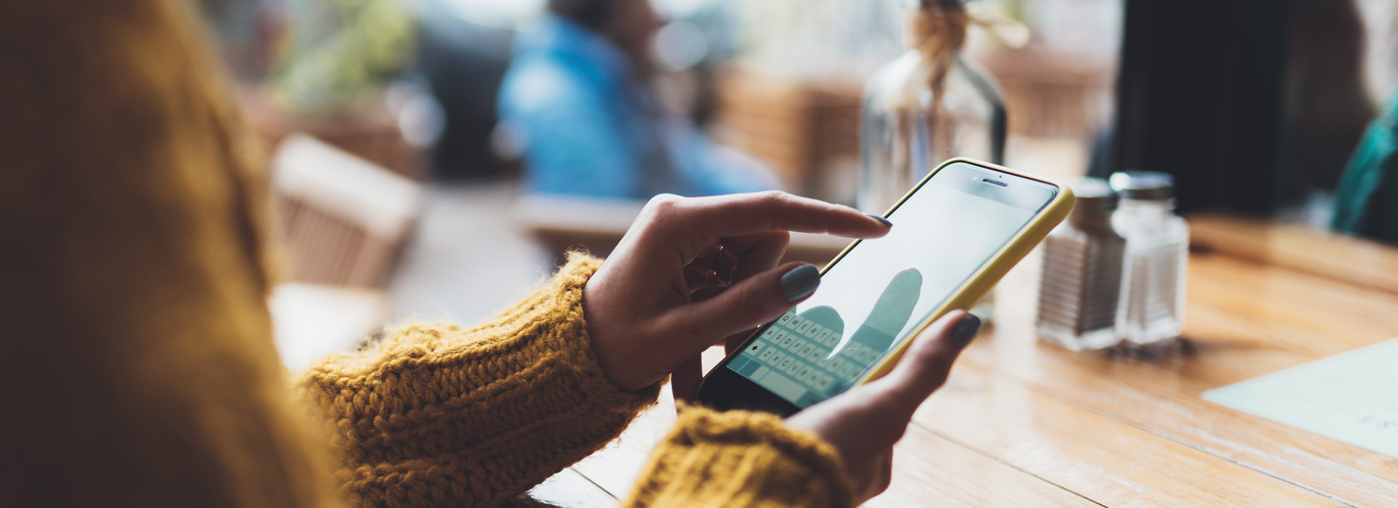 Eine Frau füllt in gemütlicher Atmosphäre in einem Restaurant ein Formular an ihrem Smartphone aus.