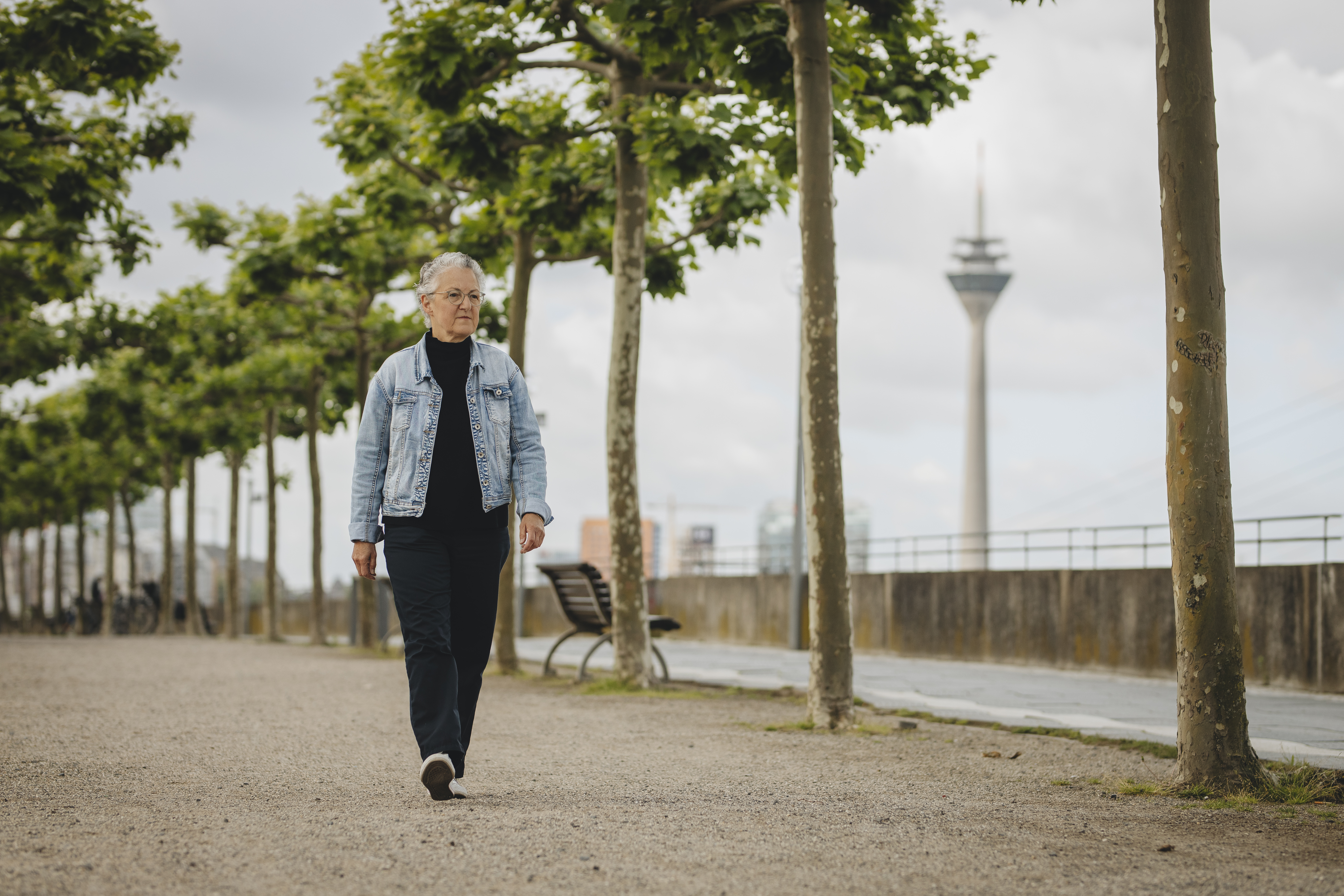 Eine Frau läuft die Rheinpromenade entlang, im Hintergrund ist der Düsseldorfer Fernsehturm zu sehen.