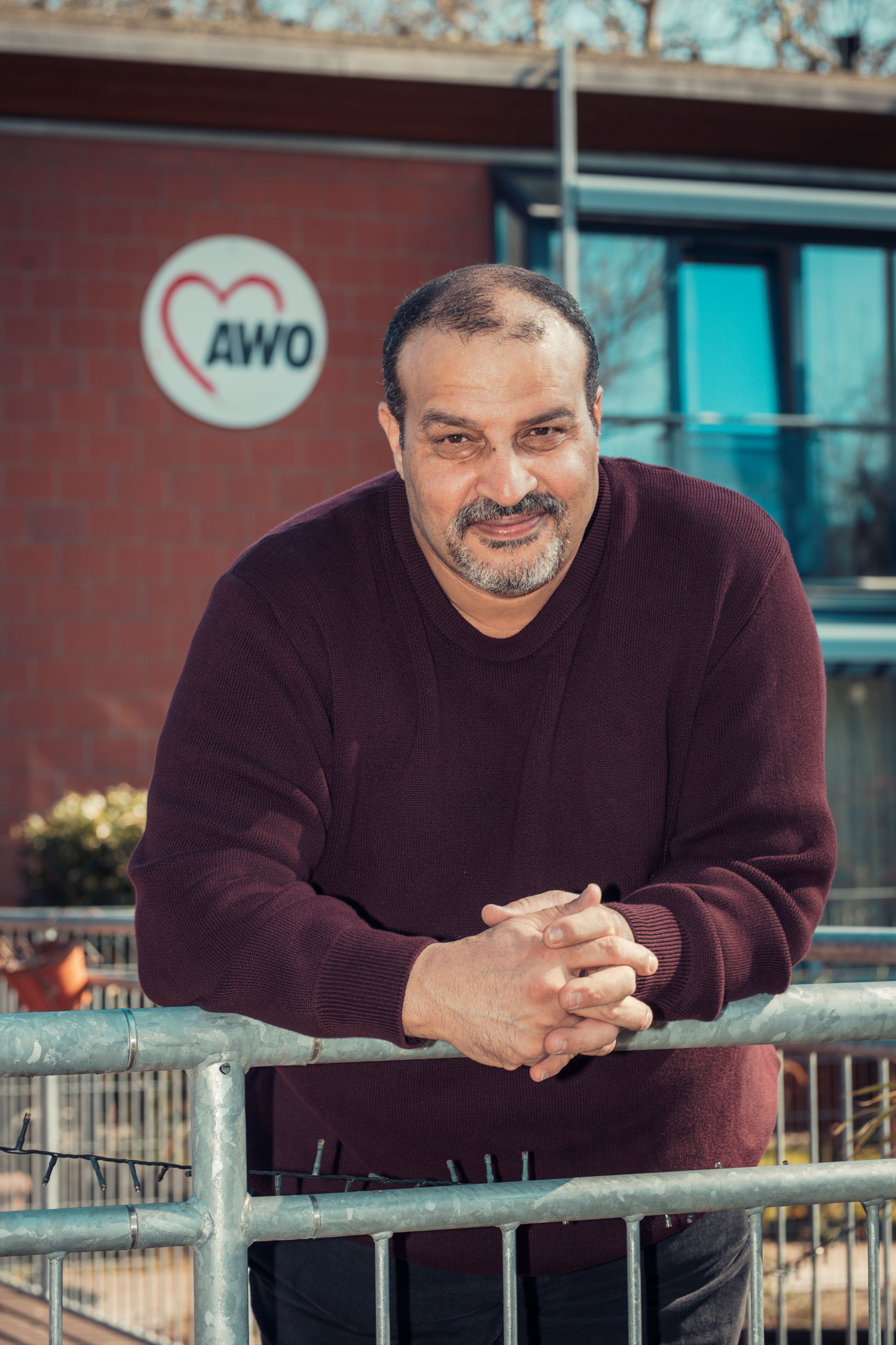 Porträt des Protagonisten der Geschichte, er lehnt an einem Geländer von einem Gebäude, hinter ihm ein AWO-Logo an der Wand.