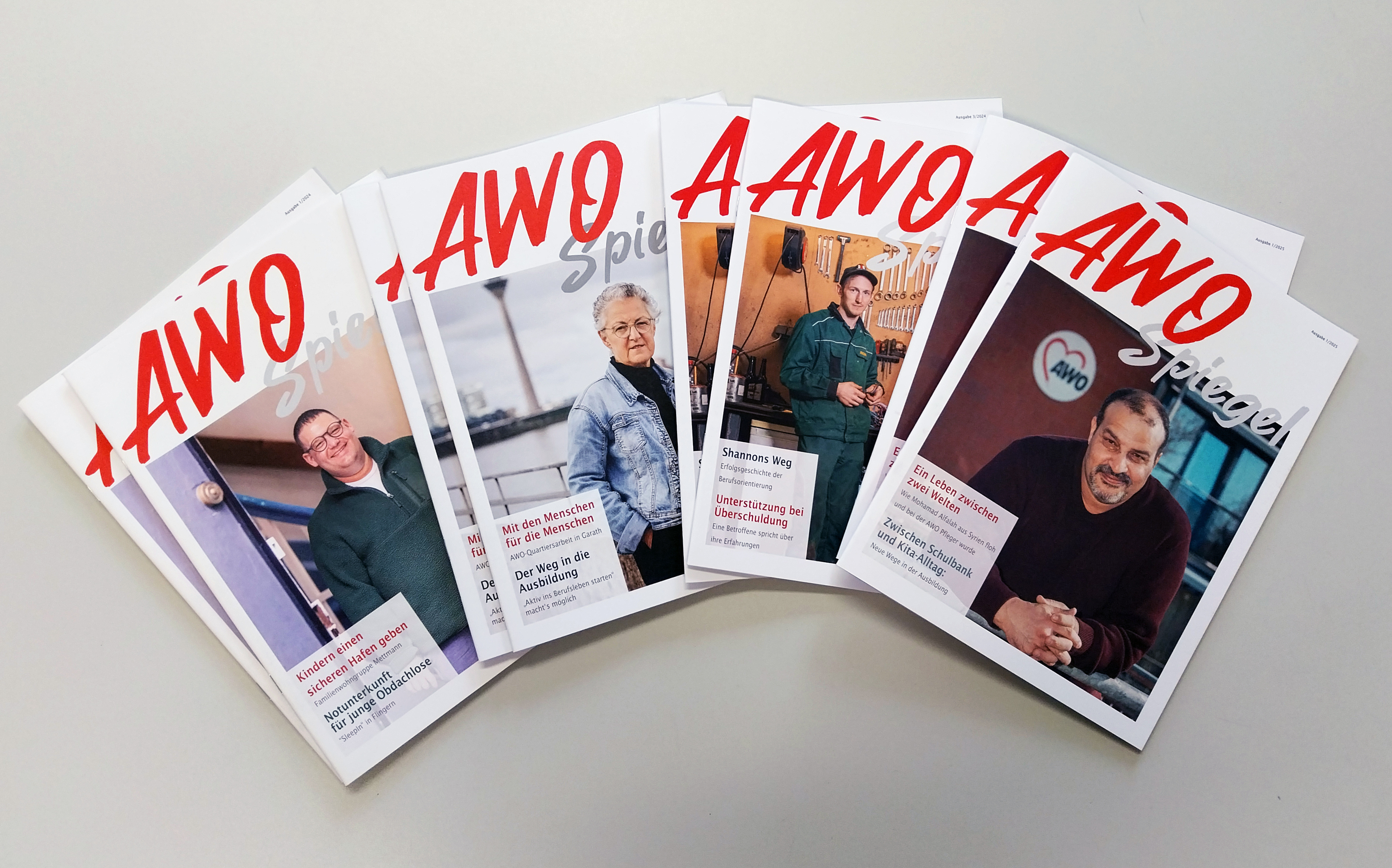 Mehrere Ausgaben des gedruckten AWOspiegels liegen aufgefächert auf einem grauen Hintergrund