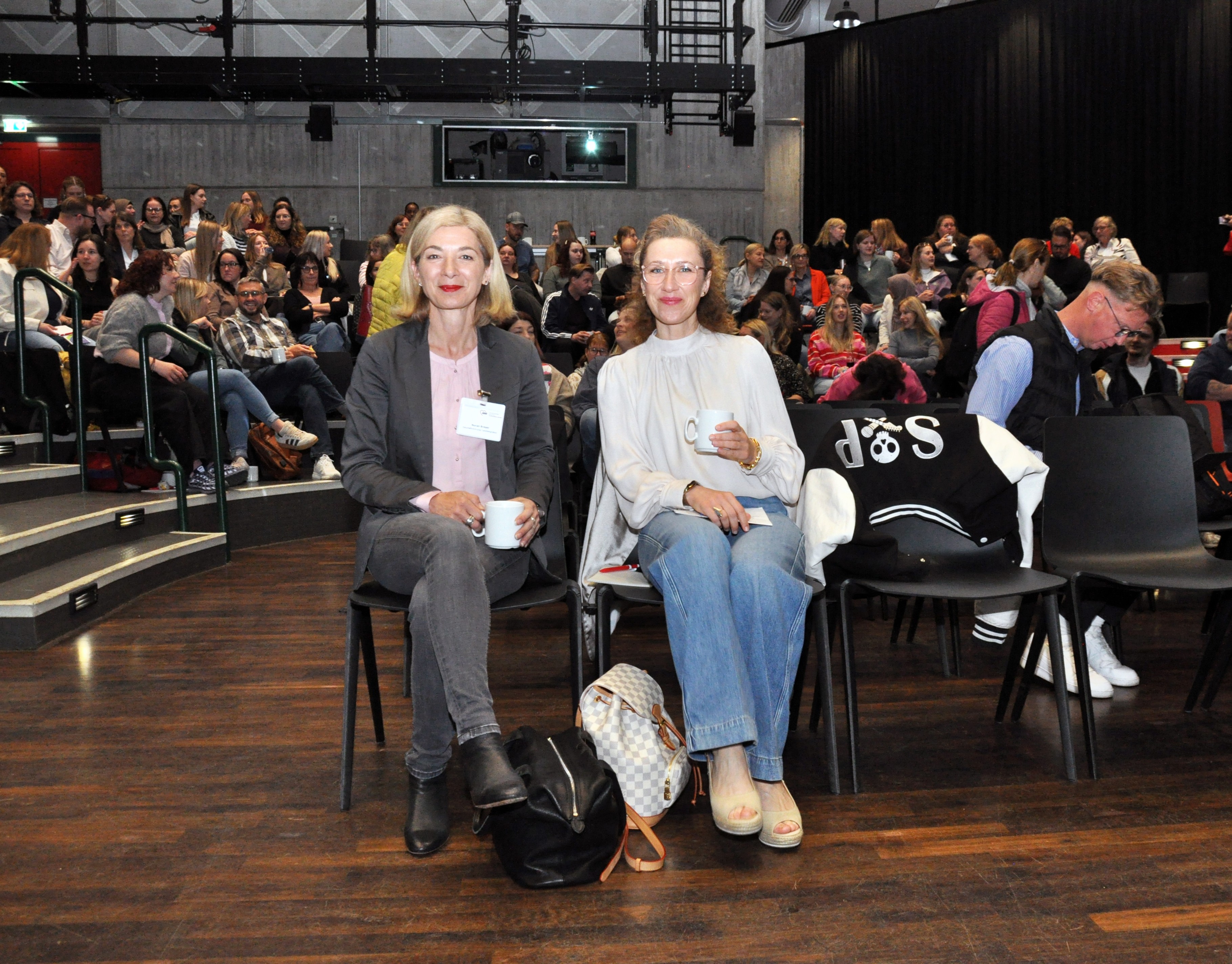 Foto von Nuran Breuer und Aleksandra Schmidt, die in der ersten Reihe des Plenums sitzen.