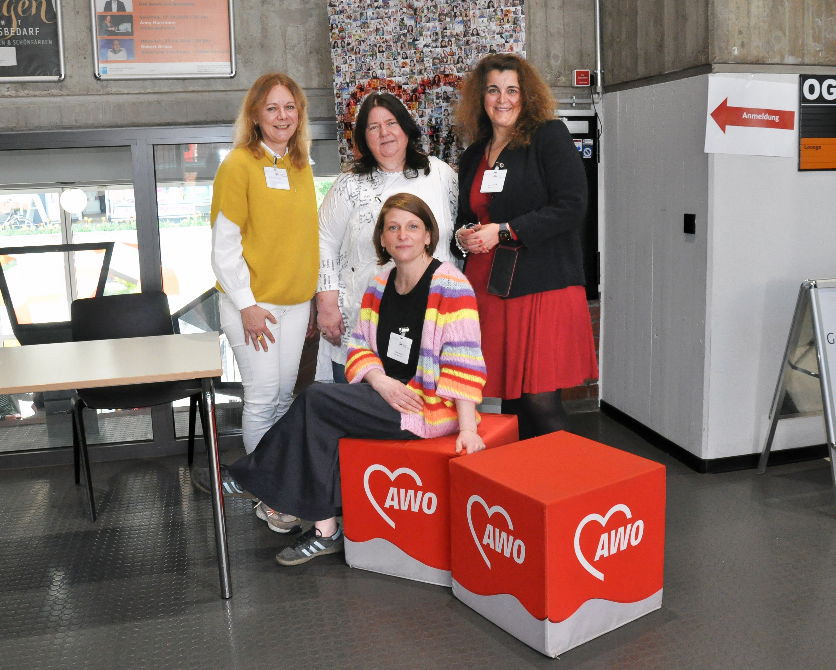 Das Organisationsteam des Fachtags, vier Personen, sitzen und stehen vor einem Rollup und zwei Sitzwürfeln mit AWO-Logos